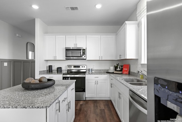 kitchen featuring light stone counters, a sink, stainless steel appliances, white cabinetry, and visible vents