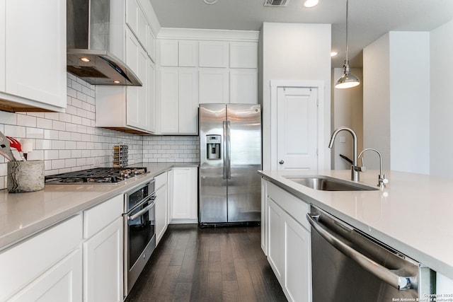 kitchen featuring light countertops, wall chimney range hood, a sink, appliances with stainless steel finishes, and dark wood-style flooring