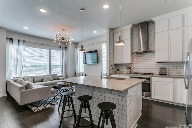 kitchen featuring a sink, dark wood finished floors, a kitchen bar, wall chimney range hood, and appliances with stainless steel finishes