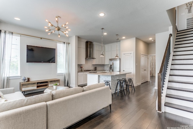 living area featuring stairs, an inviting chandelier, dark wood finished floors, baseboards, and recessed lighting