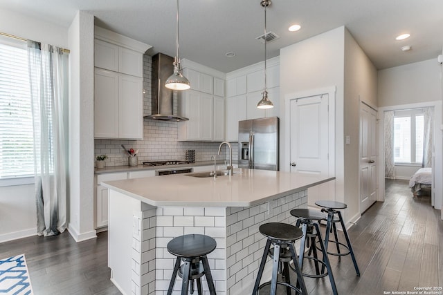 kitchen featuring stainless steel appliances, a breakfast bar, a sink, dark wood-type flooring, and wall chimney exhaust hood