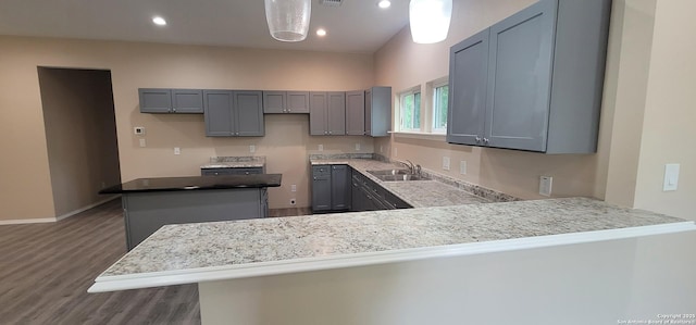kitchen featuring a peninsula, a center island, a sink, wood finished floors, and gray cabinets