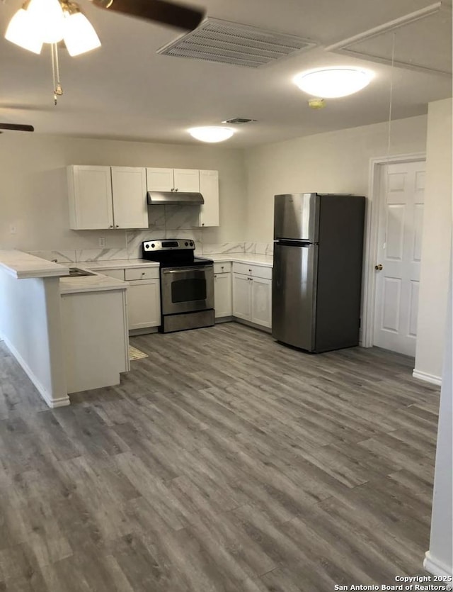 kitchen with under cabinet range hood, stainless steel appliances, light countertops, dark wood-type flooring, and a peninsula