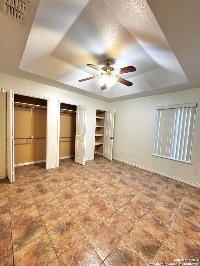 36 Leona Hts, Uvalde, TX 78801 - unfurnished bedroom featuring a raised ceiling, two closets, baseboards, and tile patterned flooring
