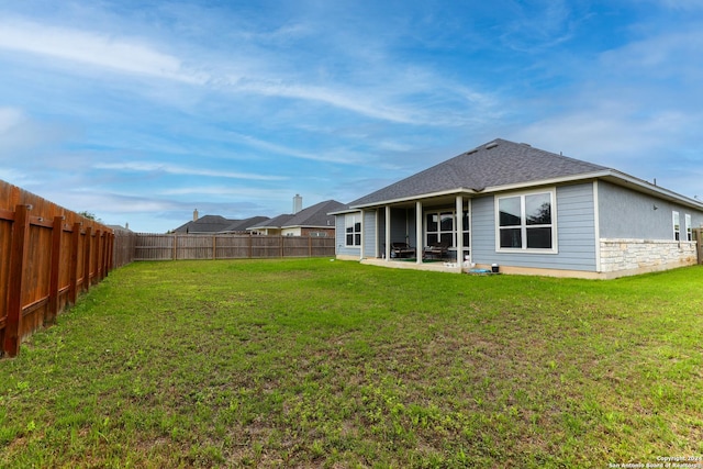 rear view of house featuring a shingled roof, a lawn, a fenced backyard, and a patio