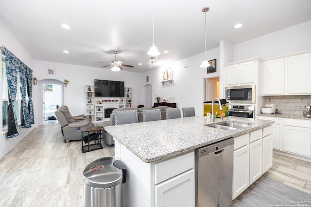 kitchen with stainless steel appliances, a sink, a center island with sink, open floor plan, and backsplash