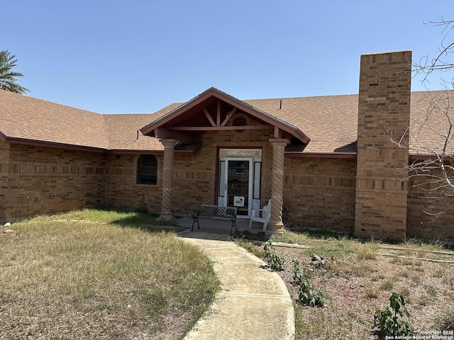 view of front of house featuring a front yard, a chimney, roof with shingles, and brick siding