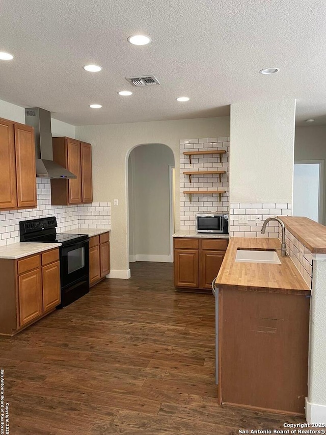 kitchen with dark wood finished floors, wall chimney range hood, a sink, stainless steel microwave, and black range with electric stovetop