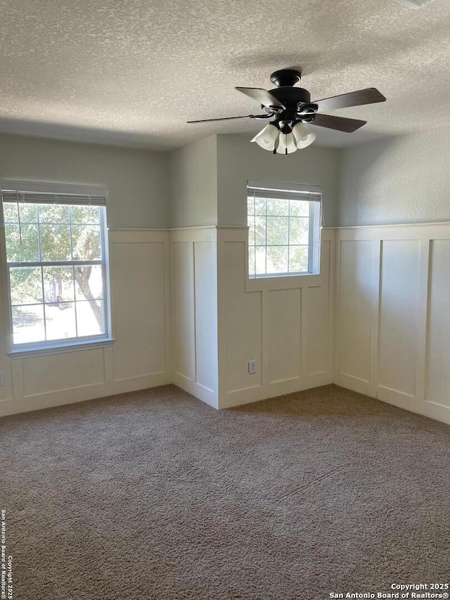 empty room with plenty of natural light, a wainscoted wall, a textured ceiling, and a decorative wall