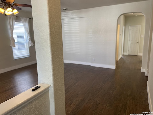 spare room with arched walkways, a ceiling fan, wood finished floors, and baseboards