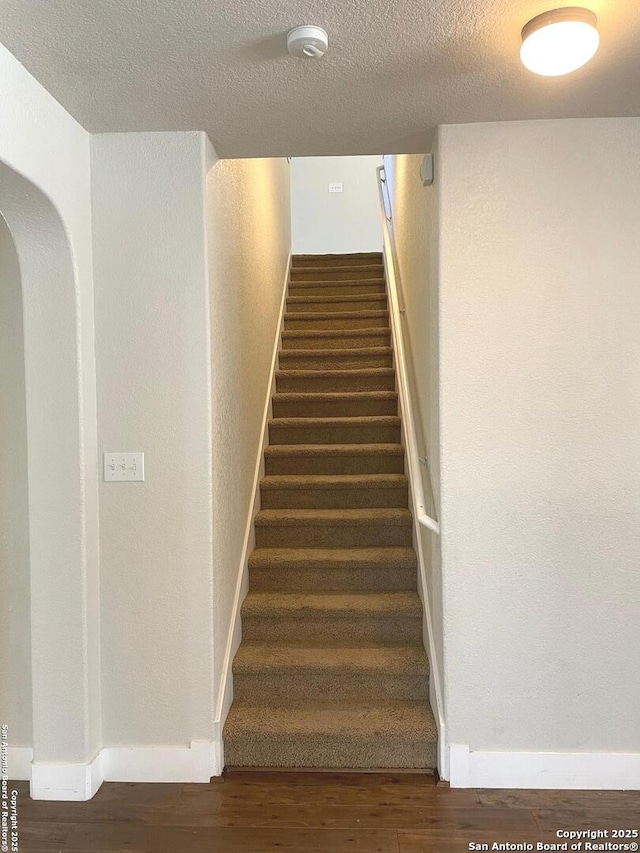 stairs with arched walkways, baseboards, wood finished floors, and a textured ceiling
