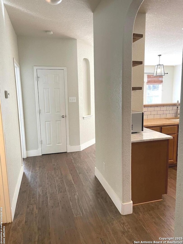 corridor featuring a sink, arched walkways, a textured ceiling, dark wood-style flooring, and baseboards