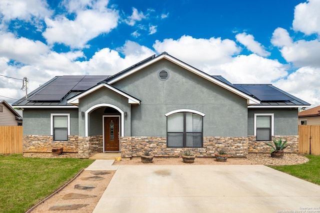 view of front of property with stucco siding, roof mounted solar panels, stone siding, and metal roof