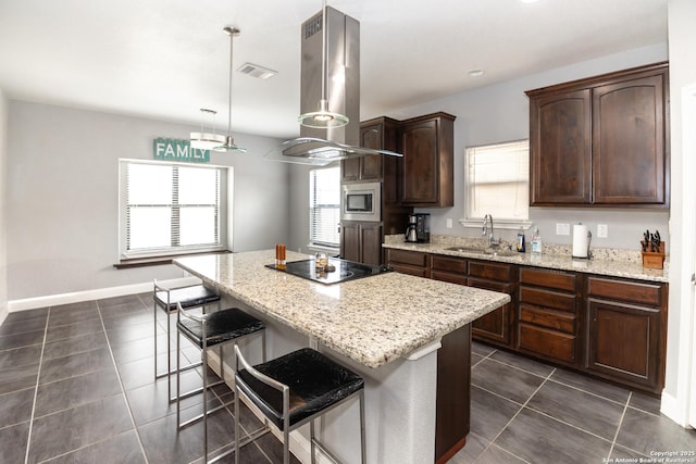 kitchen featuring dark tile patterned flooring, island exhaust hood, a sink, and stainless steel microwave