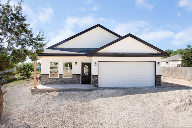 view of front of house featuring stone siding, fence, a garage, and stucco siding