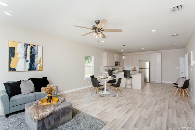 living area with baseboards, a ceiling fan, visible vents, and light wood-type flooring