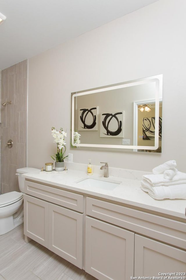 full bathroom with tiled shower, vanity, and toilet