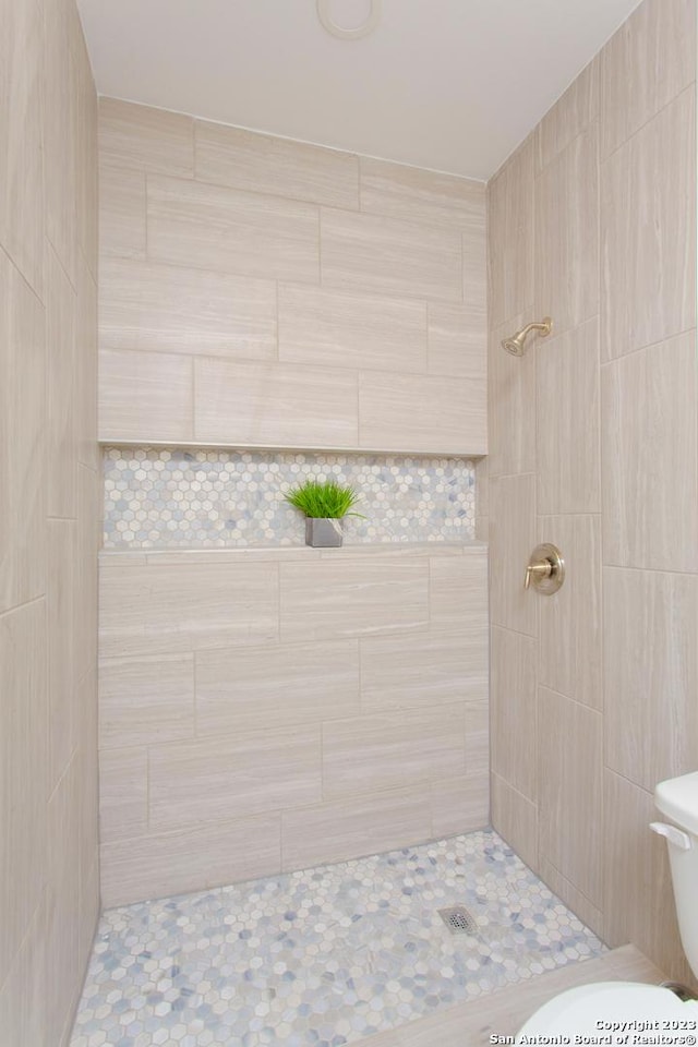 full bath with toilet, tile patterned flooring, and tiled shower