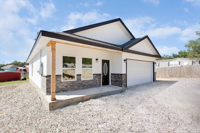 view of front of house featuring driveway, stone siding, fence, a garage, and stucco siding