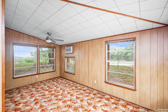 carpeted empty room with a wall mounted AC, wood walls, and ceiling fan