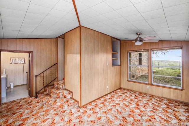 spare room featuring stairway, carpet flooring, wood walls, and ceiling fan