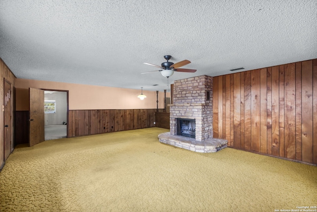 unfurnished living room with a textured ceiling, visible vents, a ceiling fan, wood walls, and a fireplace