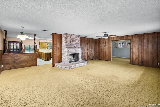unfurnished living room featuring a textured ceiling, visible vents, wood walls, ceiling fan, and a fireplace