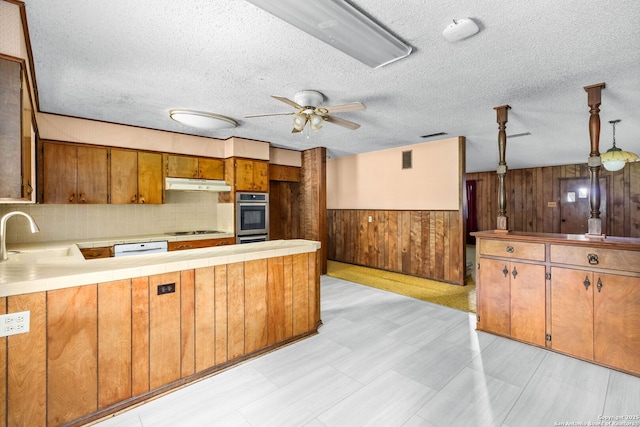kitchen featuring wood walls, under cabinet range hood, a sink, stovetop, and a peninsula