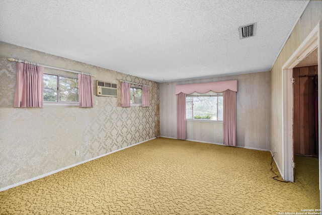 empty room featuring carpet flooring, a textured ceiling, visible vents, a wall mounted air conditioner, and wallpapered walls