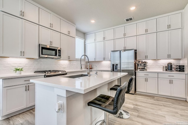 kitchen with light wood finished floors, stainless steel appliances, backsplash, light countertops, and visible vents
