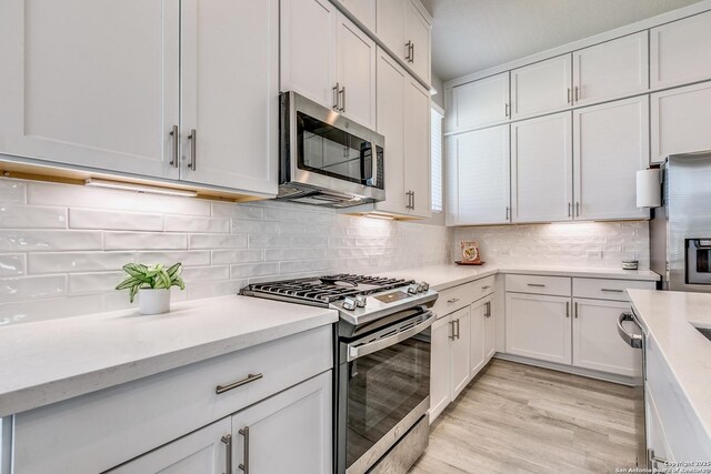 kitchen featuring light stone counters, stainless steel appliances, light wood-style flooring, white cabinets, and backsplash