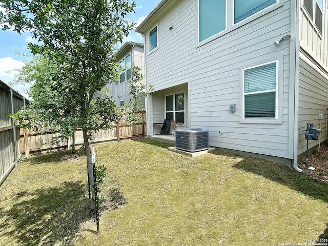 rear view of property featuring central AC, a fenced backyard, and a lawn