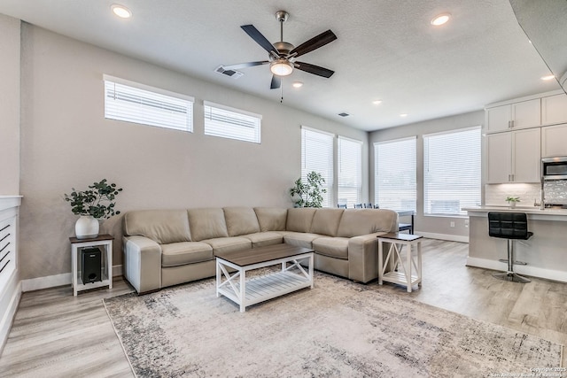 living area with baseboards, light wood-style flooring, visible vents, and ceiling fan