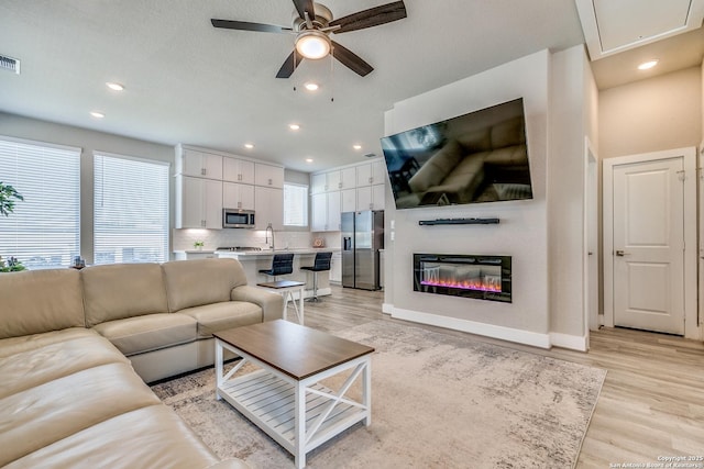 living area featuring light wood finished floors, attic access, baseboards, visible vents, and a ceiling fan