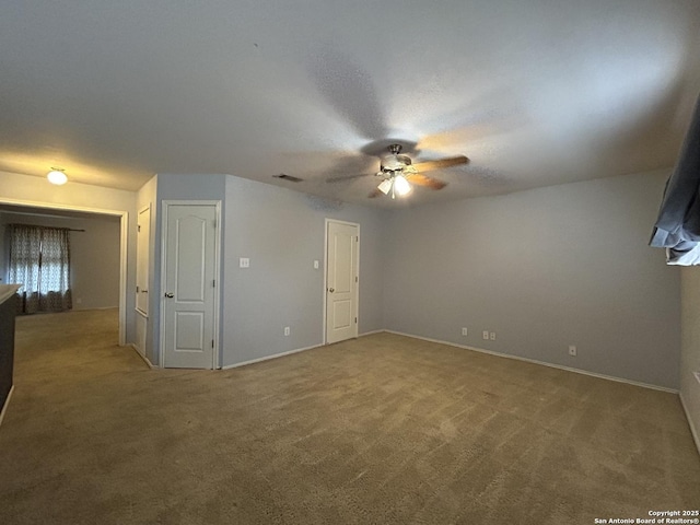 empty room with carpet floors, a ceiling fan, baseboards, and visible vents