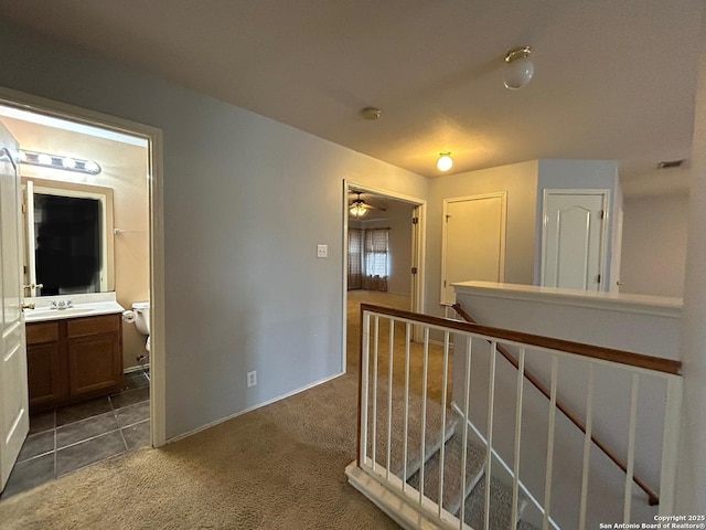 hallway with visible vents, dark carpet, baseboards, a sink, and an upstairs landing