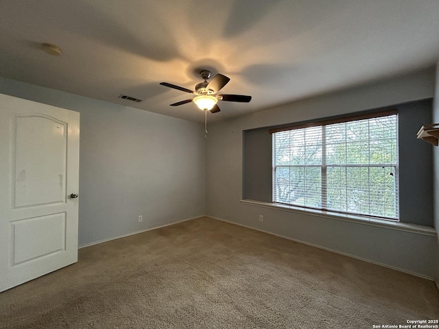 empty room featuring carpet floors, baseboards, a ceiling fan, and visible vents