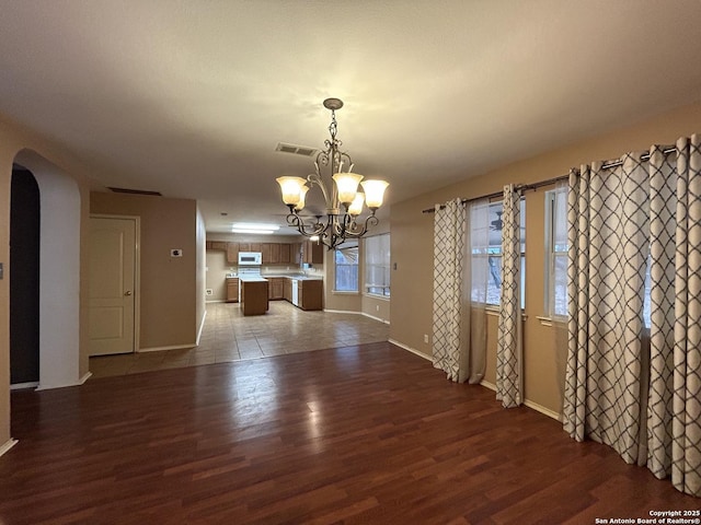 unfurnished dining area with visible vents, wood finished floors, baseboards, arched walkways, and a notable chandelier