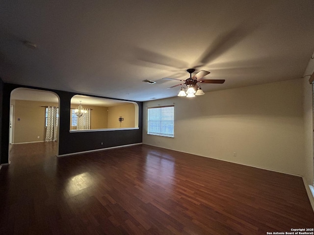 empty room featuring arched walkways, ceiling fan with notable chandelier, dark wood-style floors, and visible vents