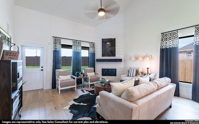 living area with high vaulted ceiling, ceiling fan, a large fireplace, and wood finished floors