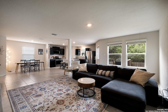 living area with a textured ceiling, visible vents, light tile patterned floors, and a healthy amount of sunlight