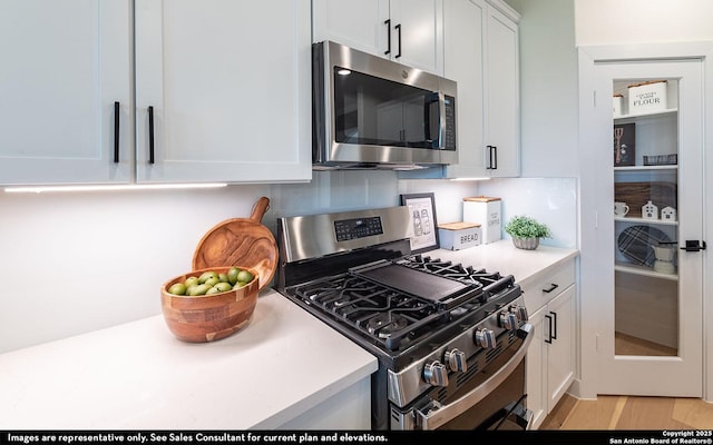 kitchen with white cabinetry, stainless steel appliances, light wood-type flooring, and light countertops