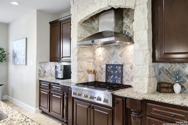 kitchen featuring wall chimney exhaust hood, stainless steel gas cooktop, baseboards, decorative backsplash, and dark brown cabinetry