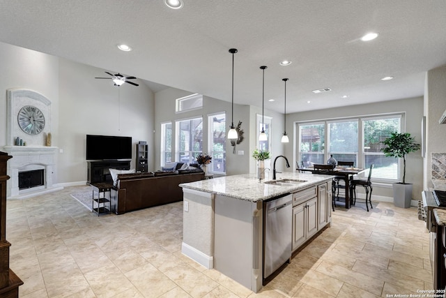 kitchen featuring a sink, stainless steel dishwasher, a fireplace, light stone counters, and a ceiling fan