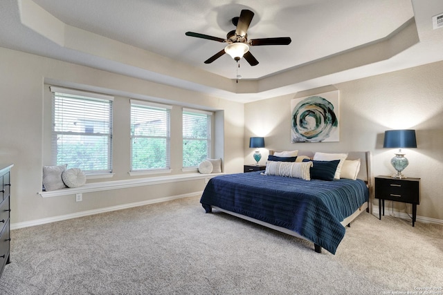 bedroom featuring carpet floors, a tray ceiling, baseboards, and a ceiling fan