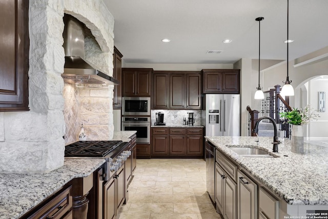 kitchen with appliances with stainless steel finishes, a sink, wall chimney range hood, arched walkways, and decorative backsplash