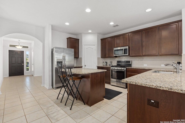 kitchen featuring a breakfast bar area, arched walkways, a sink, backsplash, and appliances with stainless steel finishes