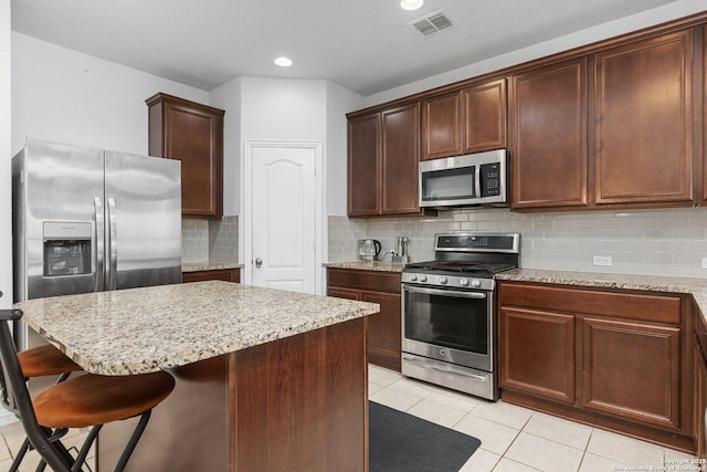 kitchen featuring light stone counters, a kitchen bar, visible vents, and stainless steel appliances