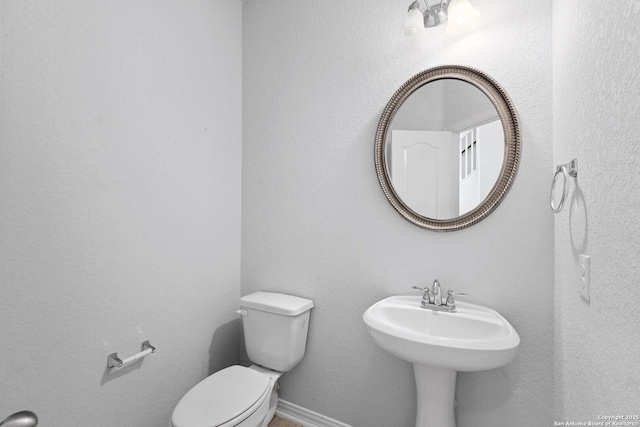 half bath featuring toilet, a sink, and baseboards