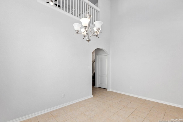 unfurnished dining area featuring arched walkways, a notable chandelier, a high ceiling, and baseboards